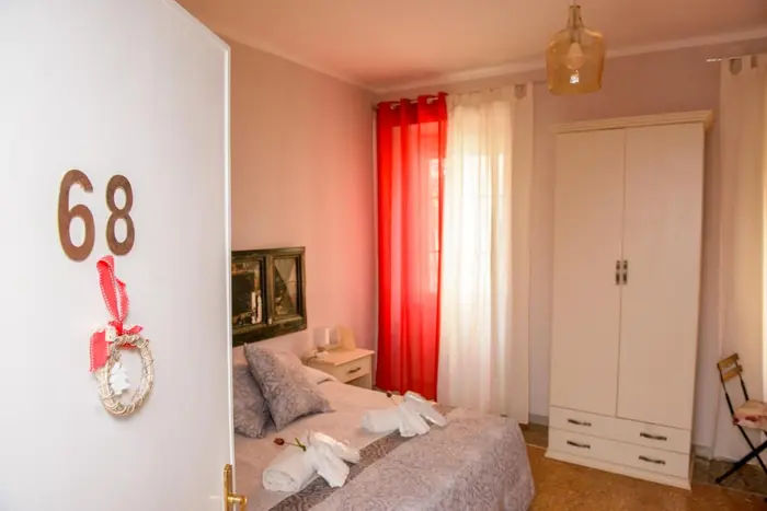 Il numero 68 sulla porta, con la ghirlanda, e dentro una camera con le tende rosse