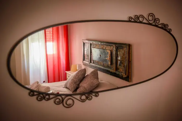 Una camera riflessa nello specchio ovale: letto, cuscini e tende rosse