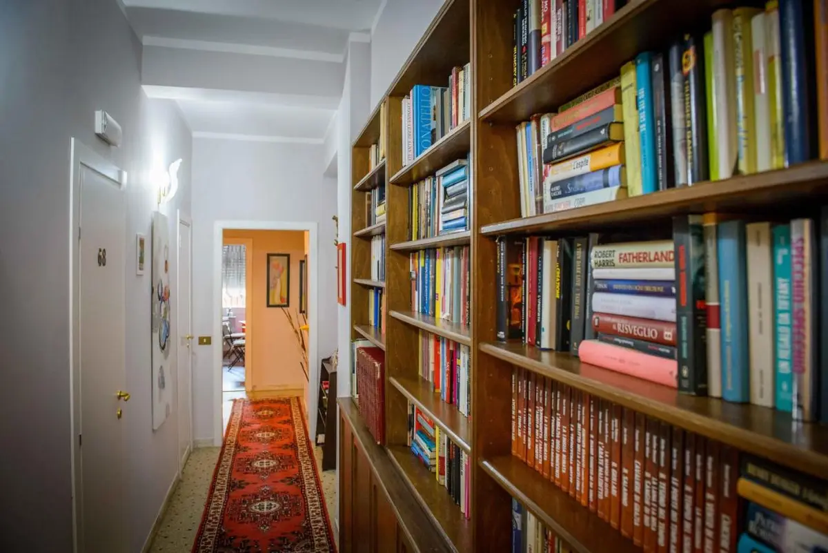 Il corridoio di Mondo Antico con la libreria a muro, piena di libri, e il tappeto rosso